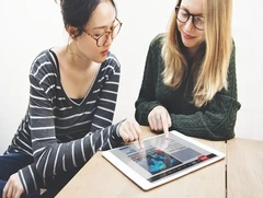 Two women reviewing data visualizations on a tablet, representing collaboration and discovering advanced features in Google Colab for data science.