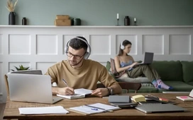 A man studying online with headphones and a laptop while taking notes, representing how flexible online learning can support career change and skill development.