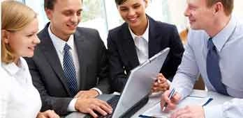 Adult learners discussing ideas around a laptop, representing mature students gaining skills and confidence through study.