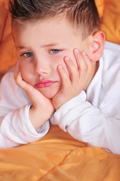 Close-up of a young child resting their face in hands, showing a thoughtful or overwhelmed mood in a home setting.
