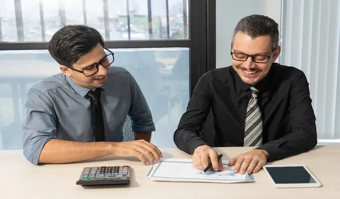 Two finance professionals reviewing documents and calculations, demonstrating key differences between bookkeeping and accounting roles.