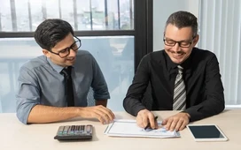 Two finance professionals reviewing documents and calculations, demonstrating key differences between bookkeeping and accounting roles.