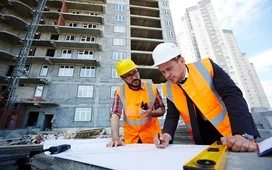 Construction managers reviewing blueprints on a building site, illustrating roles and skills taught in construction management courses.