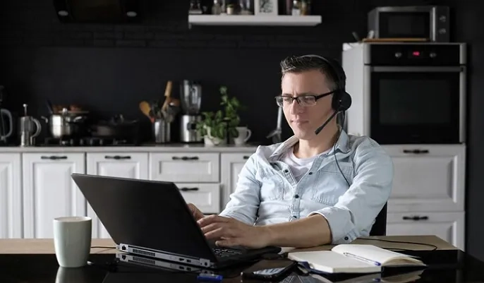 Customer service agent working from home with headset and laptop in kitchen – OHSC work-from-home guide