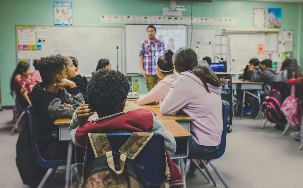 A classroom of students listening to an instructor during a lesson, representing training and education assistant qualifications.