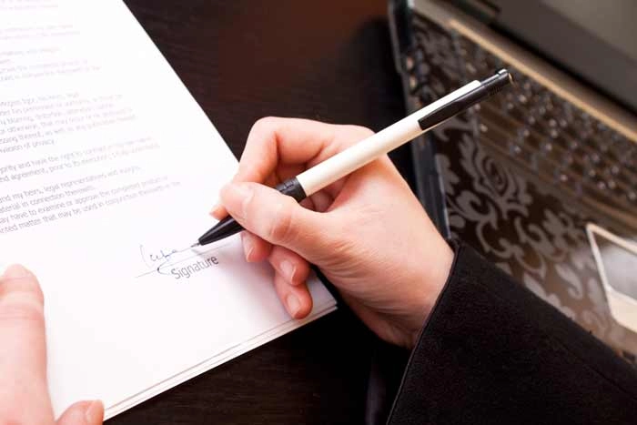Close-up of a person signing a document with a pen beside a laptop, representing essential job application tips and professional paperwork.