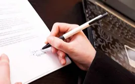 Close-up of a person signing a document with a pen beside a laptop, representing essential job application tips and professional paperwork.