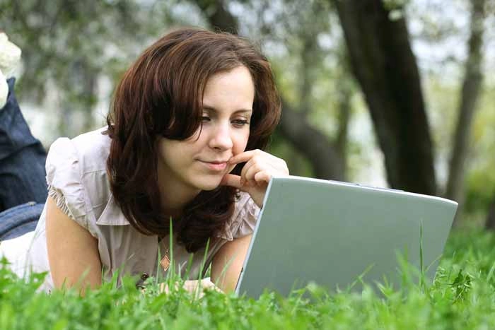 Woman studying online on a laptop while relaxing outdoors, representing convenient and flexible access to free distance learning programs.