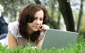 Woman studying online on a laptop while relaxing outdoors, representing convenient and flexible access to free distance learning programs.