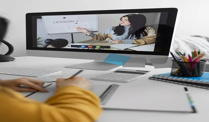 A learner taking notes while attending an online lesson on a computer, representing how free online courses with certificates can quickly enhance a resume.