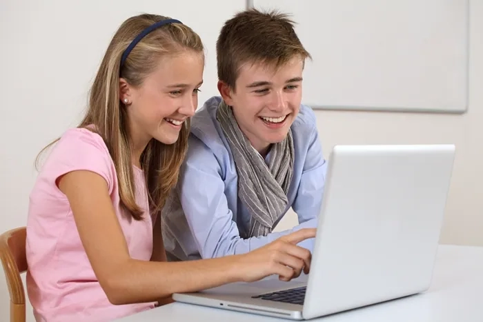 Two students smiling while learning online using a laptop, representing the value and accessibility of free online courses from UK colleges.