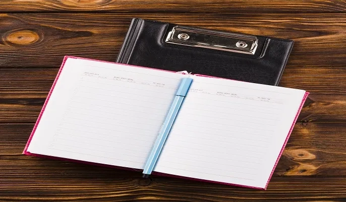 Open notebook with a pen placed on a clipboard, symbolizing note-taking and comparing tools like Google Colab and Jupyter Notebook for coding in 2024.