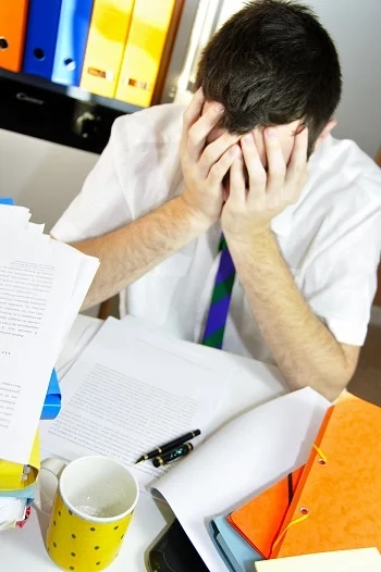 Overwhelmed adult sitting at a desk with paperwork, showing stress and difficulty coping in a busy work setting.