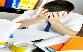 Overwhelmed adult sitting at a desk with paperwork, showing stress and difficulty coping in a busy work setting.