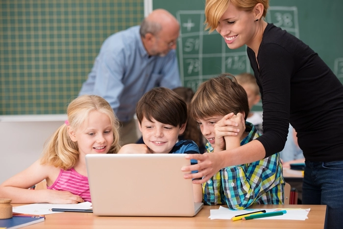 A teaching assistant helping young students learn using a laptop in a classroom, demonstrating support, guidance, and interactive learning.