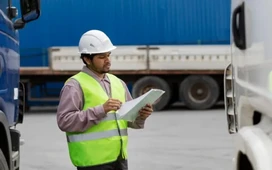 Logistics worker in safety vest checking shipment notes by trucks – logistics and transport management for global supply chains.