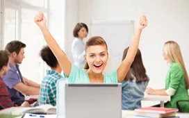 Happy student raising arms behind a laptop in a classroom, representing the accessibility and popularity of MOOCs.