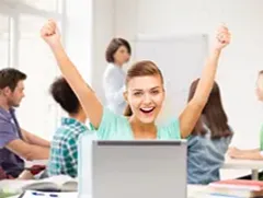 Happy student raising arms behind a laptop in a classroom, representing the accessibility and popularity of MOOCs.