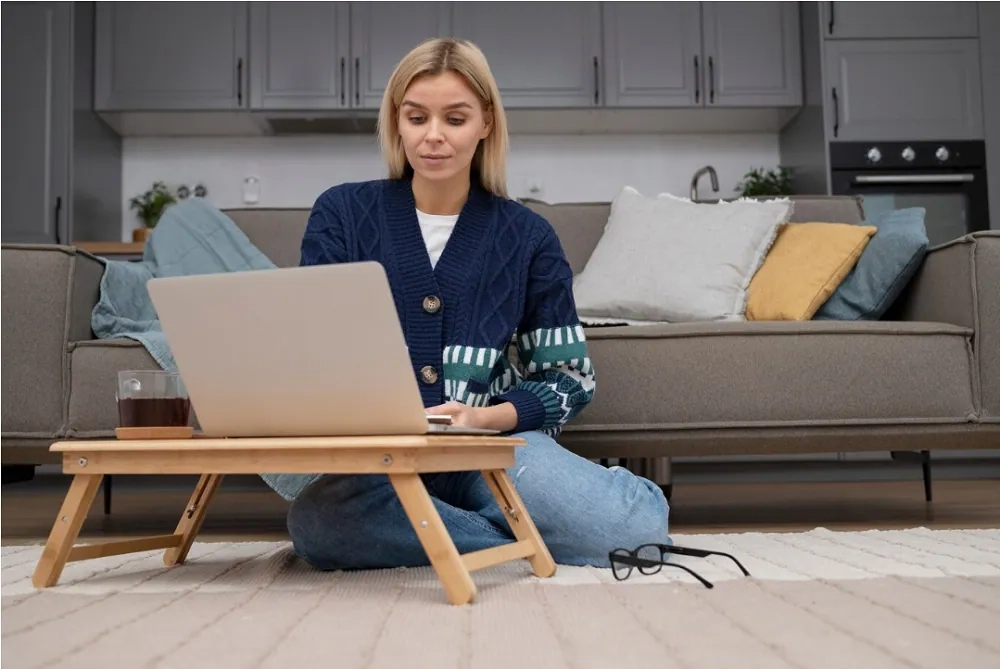 Woman working on a laptop from home on the floor – guide to mastering online work-from-home success with OHSC.