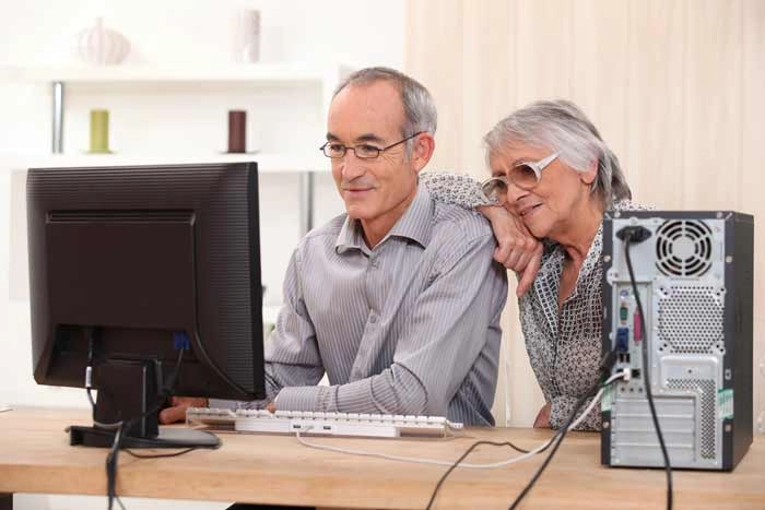 Older couple learning on a desktop computer at home, showing online study and lifelong education at any age.