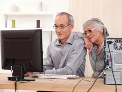 Older couple learning on a desktop computer at home, showing online study and lifelong education at any age.