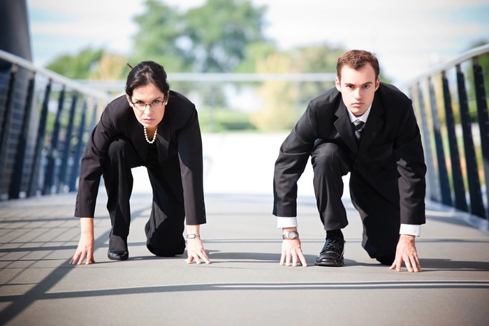 Two business professionals in a race-start pose, symbolising workplace competition and the drive to earn a promotion.