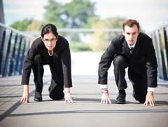 Two business professionals in a race-start pose, symbolising workplace competition and the drive to earn a promotion.