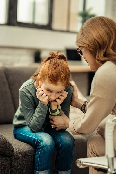 Adult comforting a sad child on a sofa, showing emotional support and early behavioural concerns in childhood development.