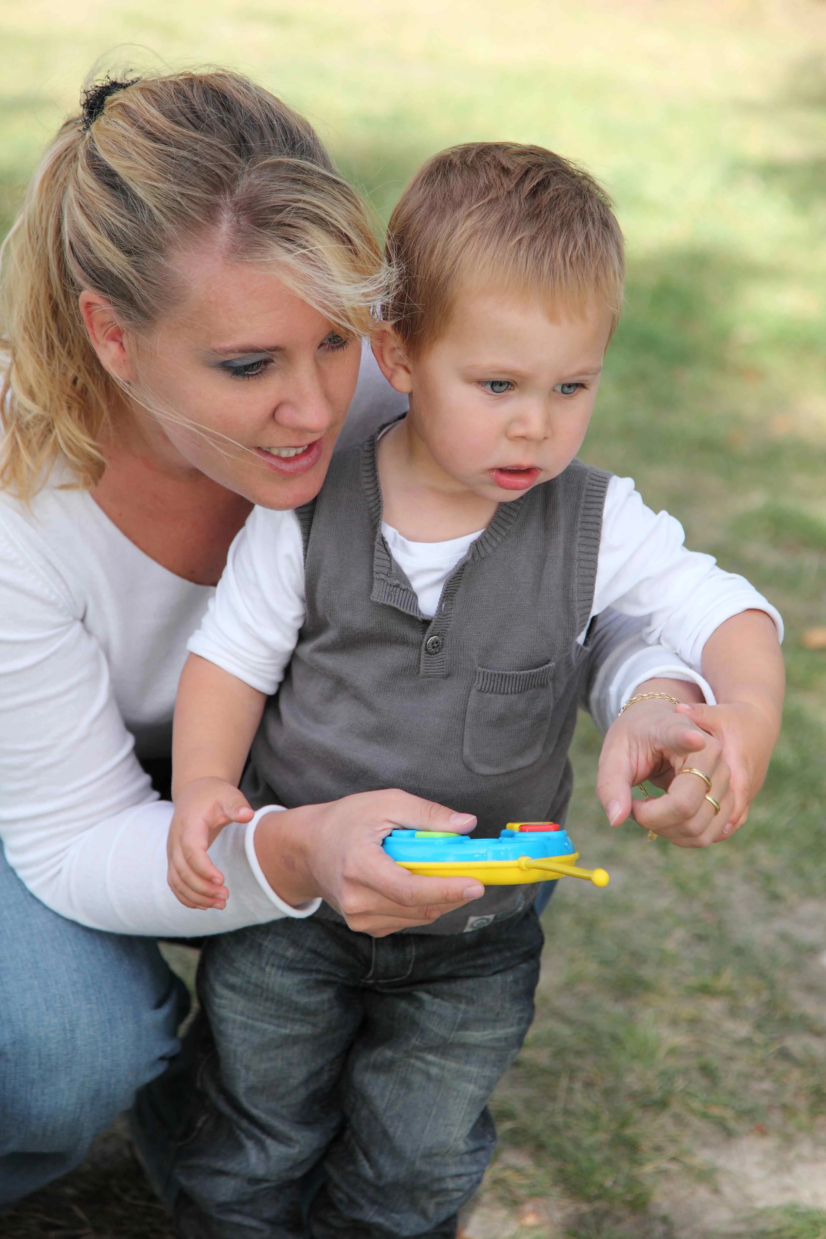 Parent guiding a young child outdoors while the child holds a toy controller, illustrating supportive interaction and early childhood development.