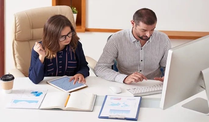 Two professionals reviewing financial records on a computer and tablet, illustrating key bookkeeping tasks for starting a career without a degree.