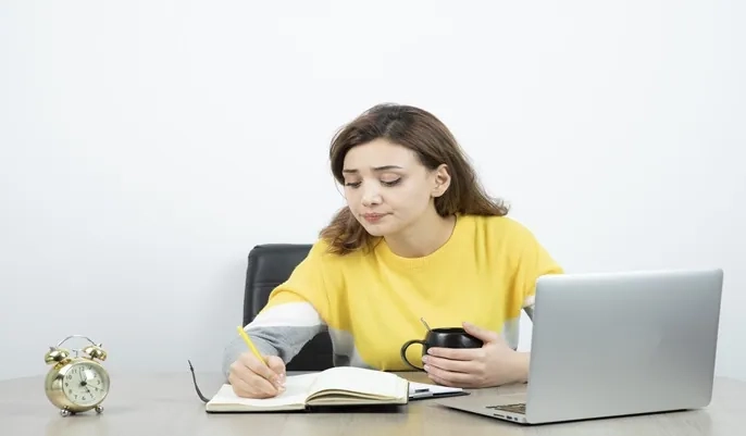A young woman studying at her desk with a laptop, notebook, and coffee, illustrating effective study habits and motivation tips for online learners.