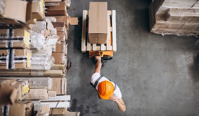 Warehouse worker moving boxes on a pallet truck, highlighting efficient inventory handling and the importance of strong warehouse management.