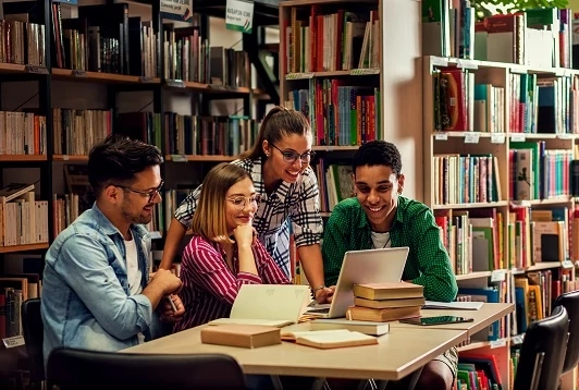 Students collaborating on a laptop in a library, illustrating what eLearning is and how online study works.