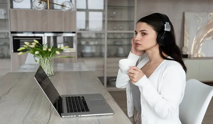 Woman wearing headphones while using a laptop at home, illustrating remote work opportunities and how to find work-from-home customer support jobs.