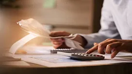 Person calculating financial figures with receipts and documents on a desk, representing foundational skills for Accounting and Finance Level 1 Award.