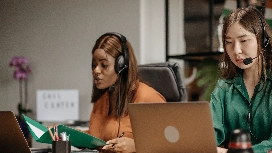 Administrative support professionals using laptops and headsets while demonstrating advanced administrative assistant skills in an office
