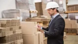 Male auditor in a warehouse checking inventory records on a clipboard, representing advanced accounting and finance concepts