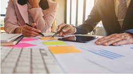 Two professionals reviewing charts, documents, and planning notes on a desk, representing strategic project management and advanced planning skills.