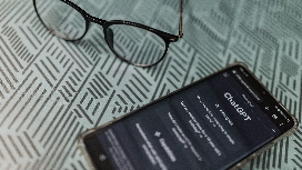 Smartphone displaying ChatGPT beside reading glasses, illustrating AI content creation and digital writing tools
