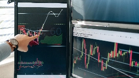 Hand pointing at market charts on dual monitors – learn AI for financial risk management in this short course