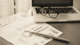 Maths and data reports beside a laptop and pen, representing OHSC’s free AI for Maths course and analytical learning.