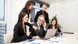 Team collaborating around a laptop to solve a business challenge, representing OHSC’s free AI in Problem Solving course.
