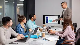 A project manager presenting data on a screen to a team with laptops, representing AI-driven planning and advanced project management strategies.