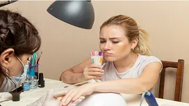 A beauty therapist providing a manicure while the client selects nail colors, demonstrating foundational Level 1 Award beauty therapy skills.