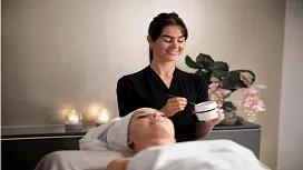 A beauty therapist preparing a facial product for a client in a calm spa setting, representing beginner Level 2 beauty therapy and salon management training.