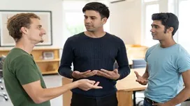 Three people engaged in a relaxed conversation, using expressive gestures that illustrate body language basics and AI-supported communication skills.