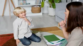 Smiling young child interacting with an adult during a simple learning activity, illustrating early development concepts in Level 1 child psychology training.