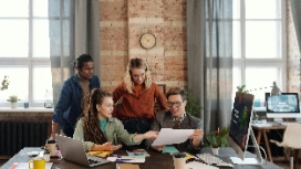 Team reviewing documents around laptops in a modern office – build practical communication skills online with OHSC