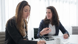 Two professionals engaged in a serious discussion at a meeting table, representing communication and mediation skills taught in conflict management training.