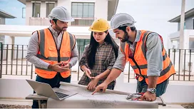 Construction team reviewing site plans outdoors with safety gear and a laptop, demonstrating foundational skills in Construction Management QLS Level 1.